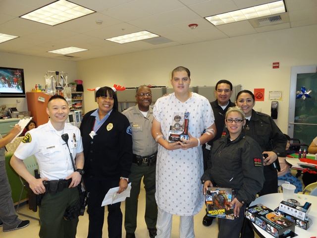 Picture of Sheriff's Personnel with Securitas Personnel next to Patient receiving a Toy.